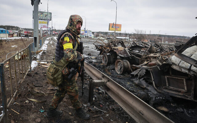 An armed Ukranian man stands by the remains of a Russian military vehicle in Bucha, close to the capital Kyiv, Ukraine, March 1, 2022. (AP Photo/Serhii Nuzhnenko)