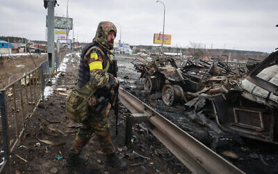 An armed man stands by the remains of a Russian military vehicle in Bucha, close to the capital Kyiv, Ukraine, March 1, 2022. (Serhii Nuzhnenko/AP)