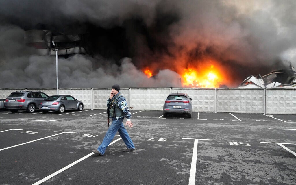 A Ukrainian serviceman walks past as fire and smoke rises over a damaged logistic center after shelling in Kyiv, Ukraine, Thursday, March 3, 2022. (AP/Efrem Lukatsky)