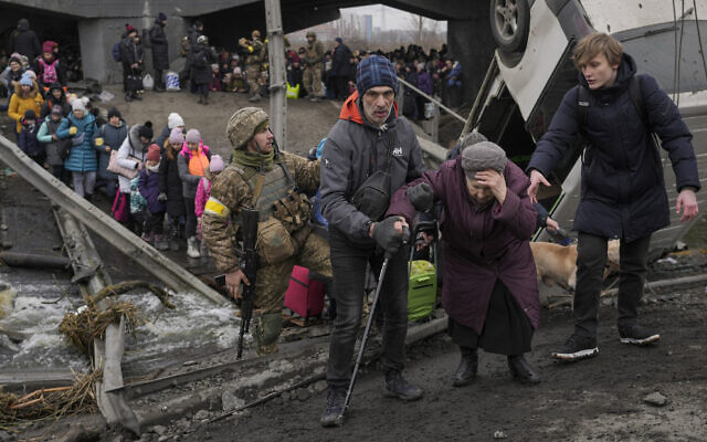 An elderly lady is assisted while crossing the Irpin river, under a bridge that was destroyed by a Russian airstrike, as civilians flee the town of Irpin, Ukraine, March 5, 2022. (AP Photo/Vadim Ghirda)