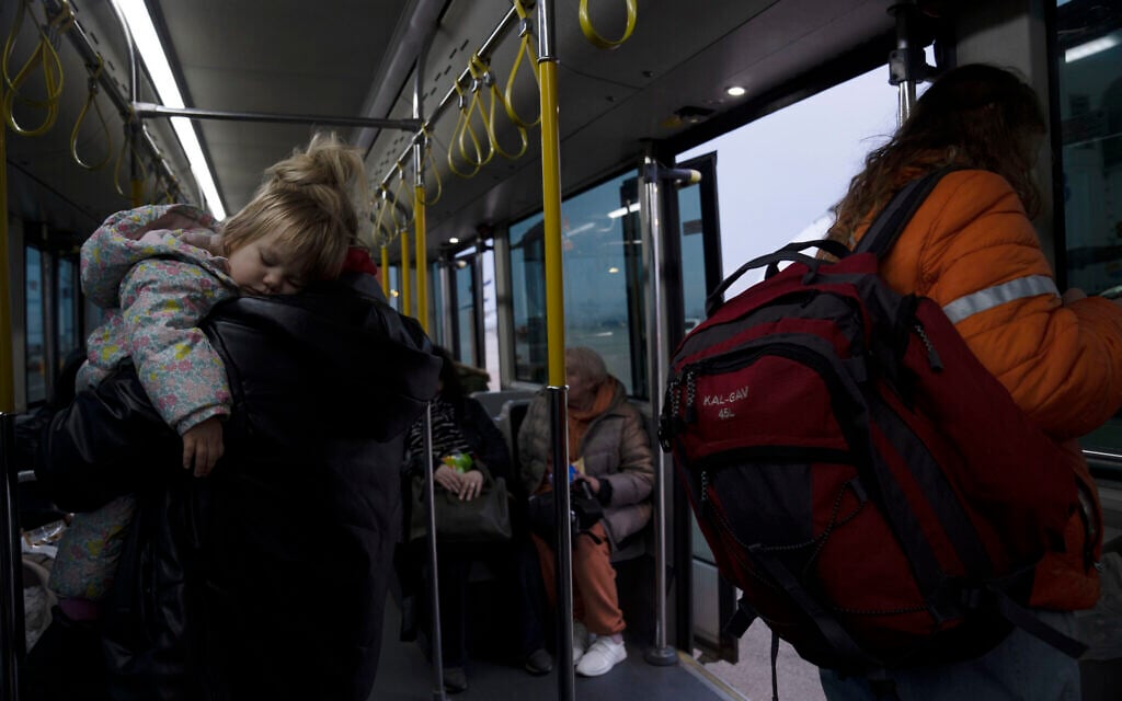 A Ukrainian toddler sleeps in her mother's arms on a shuttle bus after a special flight to Israel from Romania upon landing at Ben Gurion Airport, March 8, 2022 (AP Photo/Maya Alleruzzo)
