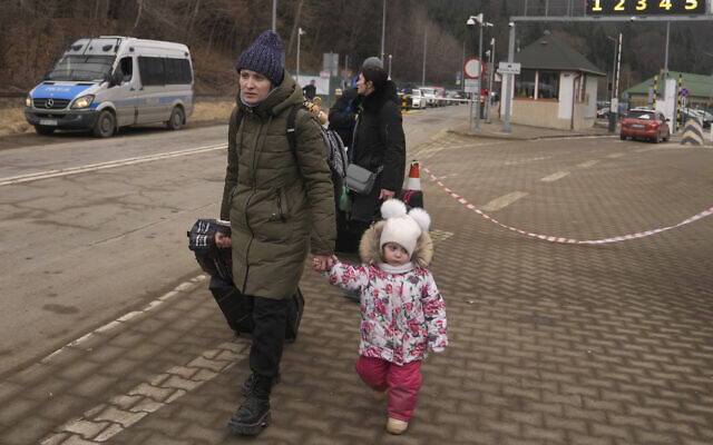A woman holds the hand of a child as she walks with others, who fled Ukraine, at the border crossing in Kroscienko, Poland, March 8, 2022 (AP Photo/Markus Schreiber)