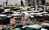A woman puts her head in her hands as she sits on a cot in a shelter, set up for displaced persons fleeing Ukraine, inside a school gymnasium in Przemysl, Poland, March 8, 2022 (AP Photo/Markus Schreiber)