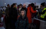 A boy stands with a group of people fleeing Ukraine as they stand in a line after arriving at the border crossing in Medyka, Poland, on Monday, March 14, 2022. (AP Photo/Petros Giannakouris)