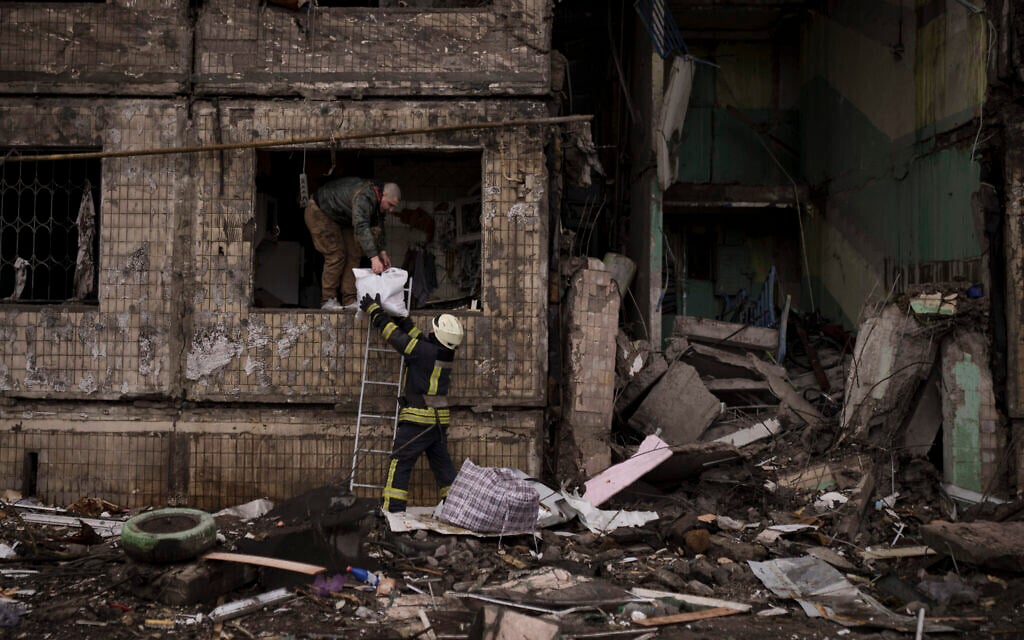 A Ukrainian firefighter helps a man remove belongings from a destroyed building after it was hit by artillery shelling in Kyiv, Ukraine, Monday, March 14, 2022. (AP/Felipe Dana)