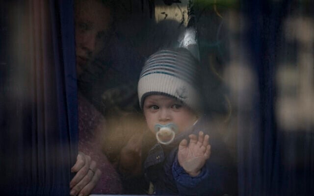 A refugee woman holds a baby while waiting on a bus for Ukrainian police to check papers and belongings in Brovary, Ukraine, March 20, 2022 (AP Photo/Vadim Ghirda)