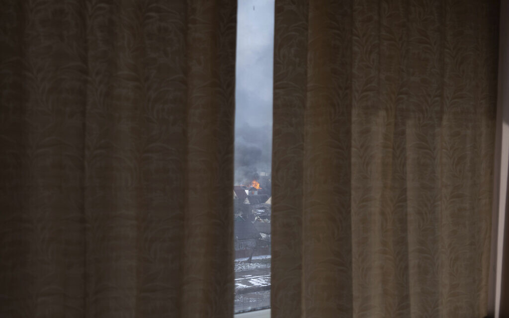 Seen through partially drawn curtains a house burns after shelling in Mariupol, Ukraine, March 12, 2022. (Mstyslav Chernov/AP)