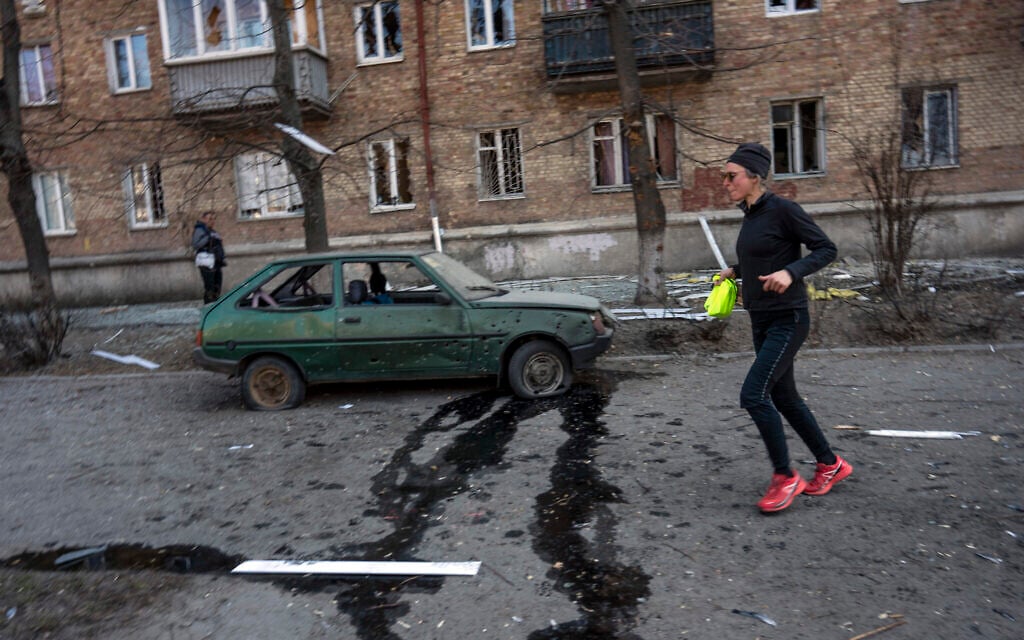 A woman exercises near a car and apartments damaged by shelling, in Kyiv, Ukraine, March 23, 2022. (AP Photo/Rodrigo Abd)