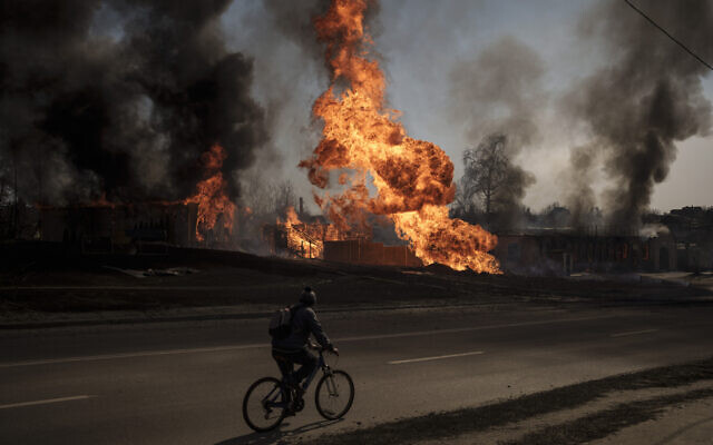 A man rides his bike past flames and smoke rising from a fire following a Russian attack in Kharkiv, Ukraine, Friday, March 25, 2022. (AP/Felipe Dana) A man rides his bike past flames and smoke rising from a fire following a Russian attack in Kharkiv, Ukraine, Friday, March 25, 2022. (AP/Felipe Dana)