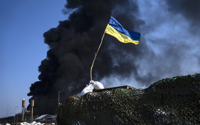 A Ukrainian flag is seen on top of a checkpoint as black smoke rises from a fuel storage of the Ukrainian army following a Russian attack, on the outskirts of Kyiv, Ukraine, on Friday, March 25, 2022. (AP/Rodrigo Abd) A Ukrainian flag is seen on top of a checkpoint as black smoke rises from a fuel storage of the Ukrainian army following a Russian attack, on the outskirts of Kyiv, Ukraine, on Friday, March 25, 2022. (AP/Rodrigo Abd)