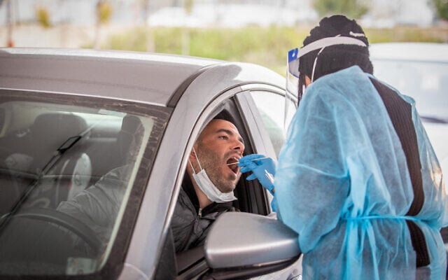A healthcare worker takes a COVID swab sample at a drive-through testing complex in Modi'in, on March 21, 2022. (Yossi Aloni/Flash90) A healthcare worker takes a COVID swab sample at a drive-through testing complex in Modi'in, on March 21, 2022. (Yossi Aloni/Flash90)