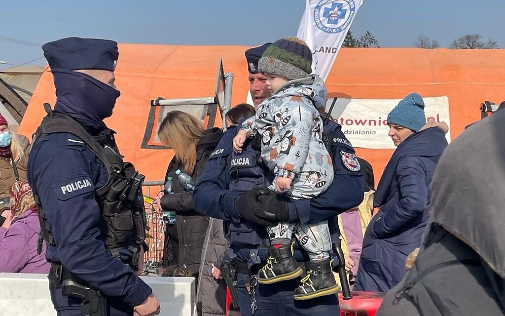 Polish police officers hold a child, in front of a line of Ukrainian refugees who just arrived on Polish soil after crossing the border into Medyka, Poland, March 15, 2022. (Carrie Keller-Lynn/The Times of Israel)