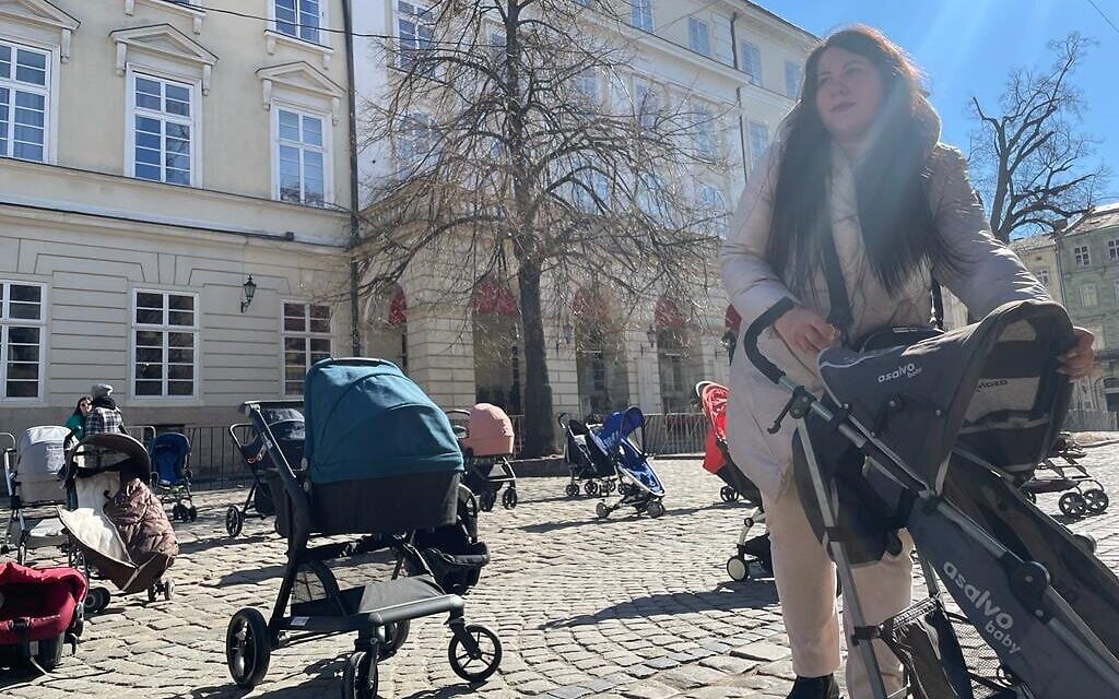 A woman arranges strollers for a demonstration against child casualties resulting from the Russian invasion of Ukraine, outside of the Lviv City Hall, March 18, 2022. (Carrie Keller-Lynn/The Times of Israel)