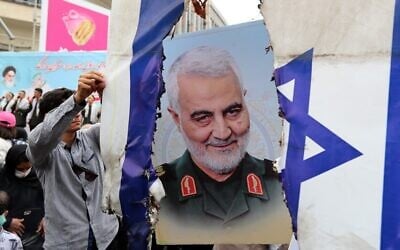 Iranians prepare to set an Israeli flag on fire next to a picture of late Iranian general Qassem Soleimani during a rally marking al-Quds Day in Tehran, Iran, on April 29, 2022. (AFP)