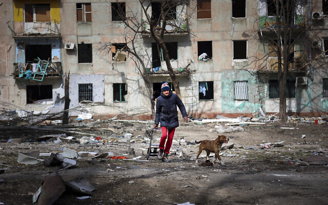 A man walks with his dog near an apartment building damaged by shelling from fighting on the outskirts of Mariupol, Ukraine, in territory under control of the separatist government of the Donetsk People's Republic, on Tuesday, March 29, 2022. (AP Photo/Alexei Alexandrov)