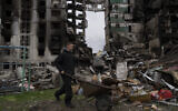 A young man pushes a wheelbarrow in front of a destroyed apartment building in the town of Borodyanka, Ukraine, on Sunday, April 10, 2022. (AP Photo/Petros Giannakouris)