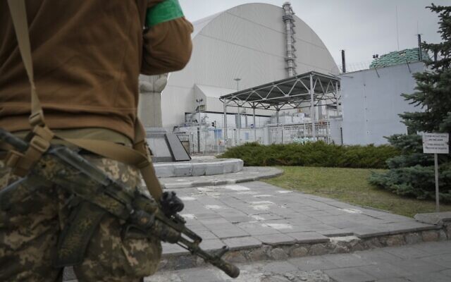 A Ukrainian soldier stands against the background of a shelter above the sarcophagus covering the exploded reactor at the Chernobyl nuclear power plant in Chernobyl, Ukraine, April 16, 2022. (AP Photo/Efrem Lukatsky)