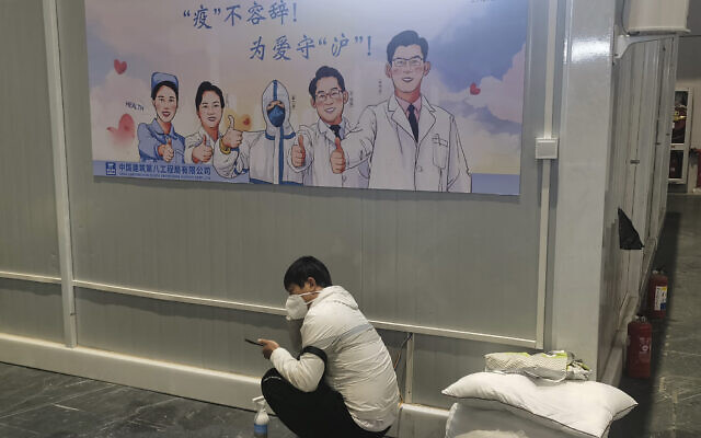 A resident staying at a temporary hospital converted from the National Exhibition and Convention Center to quarantine COVID-positive people squats near a propaganda poster calling for action against the pandemic in Shanghai, China on April 18, 2022.(Chinatopix via AP) A resident staying at a temporary hospital converted from the National Exhibition and Convention Center to quarantine COVID-positive people squats near a propaganda poster calling for action against the pandemic in Shanghai, China on April 18, 2022.(Chinatopix via AP)