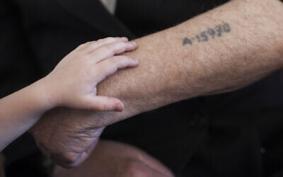 In this illustrative image, a little boy puts his hand on his grandfather's prisoner number tattooed on his arm in Jerusalem on May 24, 2013. (Yonatan Sindel/Flash90)