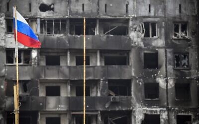 A Russian national flag flies by destroyed buildings in Mariupol on April 12, 2022, as Russian troops intensify a campaign to take the strategic port city. *EDITOR'S NOTE: This picture was taken during a trip organized by the Russian military.* (Photo by Alexander NEMENOV / AFP)