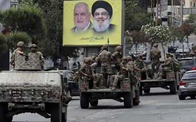 Lebanese army vehicles drive past a sign showing the images of (R to L) the leader of the Lebanese Shiite Muslim movement Hezbollah Hassan Nasrallah and the movement's parliamentary candidate Mohammed Fneish, along a road while on patrol in the southern city of Nabatiyeh, on May 15, 2022 during the national parliamentary elections. (Mahmoud Zayyat/AFP)