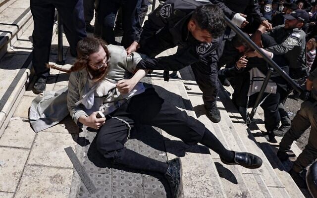 An ultra-Orthodox man pilgrim lies on the ground during scuffles with police as they try to limit entry to the grave site of Rabbi Shimon Bar Yochai at Mount Meron, during the Lag B'Omer holiday that commemorates the 2nd-century Jewish scholar's death, May 19, 2022. (Menahem KAHANA / AFP)