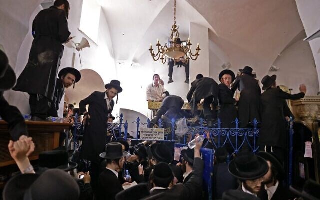 Ultra-Orthodox Jews climb over a fence to reach the tomb of Rabbi Shimon Bar Yochai at Mount Meron, following earlier scuffles with police who tried to prevent them from entering the gravesite, during the holiday of Lag B'Omer that commemorates the Jewish 2nd Century scholar's death, on May 19, 2022. (Menahem KAHANA / AFP)