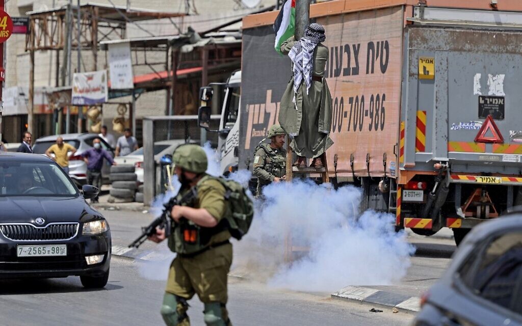 Illustrative: A man hangs a Palestinian flag on a lamppost in the northern West Bank town of Huwara amid clashes with Israeli troops on May 29, 2022. (Jaafar Ashtiyeh/AFP) Illustrative: A man hangs a Palestinian flag on a lamppost in the northern West Bank town of Huwara amid clashes with Israeli troops on May 29, 2022. (Jaafar Ashtiyeh/AFP)