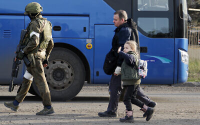 A man and a girl who left a shelter in the Metallurgical Combine Azovstal walk to a bus escorted by Russian Army serviceman in Mariupol, eastern Ukraine, on Friday, May 6, 2022. (AP Photo/Alexei Alexandrov)