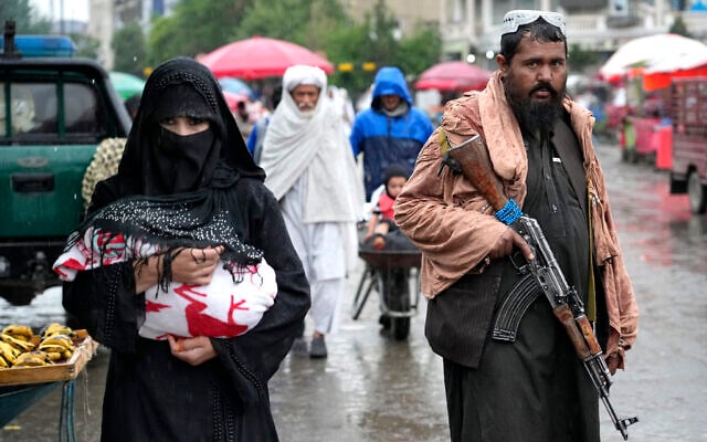 An Afghan woman walks through the old market as a Taliban fighter stands guard, in downtown Kabul, Afghanistan, May 3, 2022. (AP Photo/Ebrahim Noroozi)