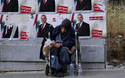 A homeless woman sits in front of campaign posters for a candidate in the upcoming parliamentary elections in Beirut, Lebanon, May 9, 2022. (AP Photo/Hassan Ammar)