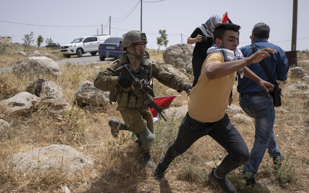An Israeli soldier chases a protester while Palestinian, Israeli and foreign peace activists attempt to open a road that passes close to the Israeli outpost of Mitzpe Yair to Masafer Yatta in the West Bank on May 13, 2022. (AP Photo/Nasser Nasser) An Israeli soldier chases a protester while Palestinian, Israeli and foreign peace activists attempt to open a road that passes close to the Israeli outpost of Mitzpe Yair to Masafer Yatta in the West Bank on May 13, 2022. (AP Photo/Nasser Nasser)
