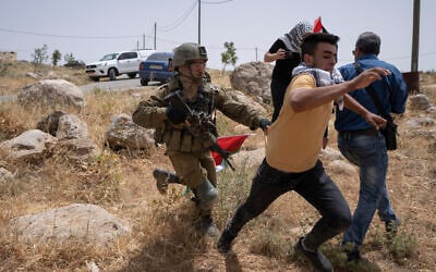 An Israeli soldier chases a protester while Palestinian, Israeli and foreign peace activists attempt to open a road that passes close to the Israeli outpost of Mitzpe Yair to Masafer Yatta in the West Bank on May 13, 2022. (AP Photo/Nasser Nasser)