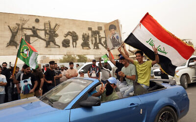 Followers of Shiite cleric Muqtada al-Sadr hold a poster with his photo and wave an Iraqi flag as they celebrate the passing of a law criminalizing the normalization of ties with Israel, in Tahrir Square, Baghdad, Iraq, Thursday, May 26, 2022. (AP Photo/Hadi Mizban)