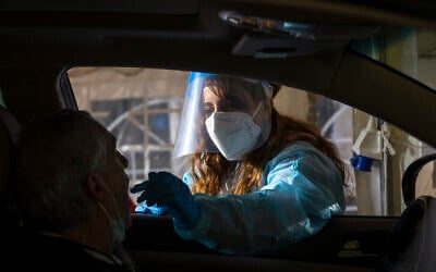 A Magen David Adom health worker take a swab sample from at a drive-thru COVID-19 testing complex in Jerusalem, on March 22, 2022. (Olivier Fitoussi/Flash90)