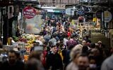 Illustrative: People shop at the Jerusalem Mahane Yehuda market, during the Jewish holiday of Passover, April 19, 2022. (Yonatan Sindel/Flash90)