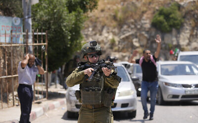 An Israeli soldier draws his weapon as mourners attending the funeral for Auda Sadaqa, 17, react at a checkpoint in the West Bank village of Al-Madiya near Ramallah, Friday, June 3, 2022. (AP/ Majdi Mohammed)