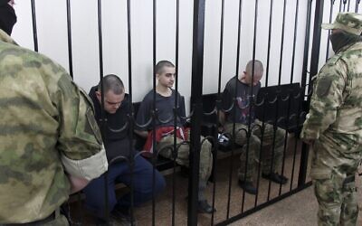 Two British citizens Aiden Aslin, left, and Shaun Pinner, right, and Moroccan Saaudun Brahim, center, sit behind bars in a courtroom in Donetsk, in the territory which is under the Government of the Donetsk People's Republic control, eastern Ukraine, Thursday, June 9, 2022. (AP Photo)