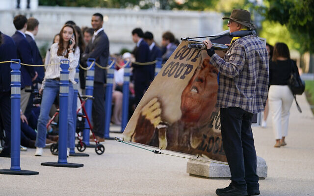 An activist holds a sign next to a line of people waiting to enter the Cannon Building, Thursday, June 9, 2022, in Washington. (AP Photo/Julio Cortez)