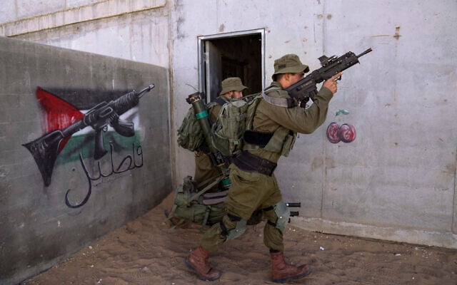 Israeli soldier carry ammunition next to a graffiti featuring the Palestinian flag, during an urban warfare exercise at an army training facility at the Tzeelim army base, southern Israel, May 25, 2022. (Oded Balilty/AP)