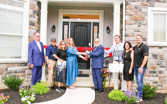 Rabbi Yosef and Chana Lipsker, fourth an fifth from left, cut the ribbon in front of the new Chabad hospitality center. (Courtesy)