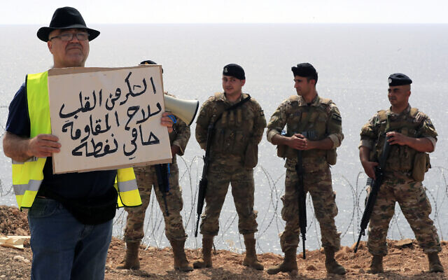 A Lebanese activist holds a placard in Arabic that reads "Thank you from the heart to the weapons of the resistance, protectors of the oil," as Lebanese soldiers stand guard during a protest in the southern border town of Naqoura, Lebanon, Saturday, June 11, 2022. (AP/Mohammed Zaatari) A Lebanese activist holds a placard in Arabic that reads "Thank you from the heart to the weapons of the resistance, protectors of the oil," as Lebanese soldiers stand guard during a protest in the southern border town of Naqoura, Lebanon, Saturday, June 11, 2022. (AP/Mohammed Zaatari)