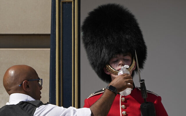 A police officer givers water to a British soldier wearing a traditional bearskin hat, on guard duty outside Buckingham Palace, during hot weather in London, July 18, 2022 (AP Photo/Matt Dunham) A police officer givers water to a British soldier wearing a traditional bearskin hat, on guard duty outside Buckingham Palace, during hot weather in London, July 18, 2022 (AP Photo/Matt Dunham)