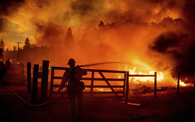 A firefighter extinguishes flames as the Oak Fire crosses Darrah Rd. in Mariposa County, California, on July 22, 2022. Crews were able to to stop it from reaching an adjacent home. (AP Photo/Noah Berger)