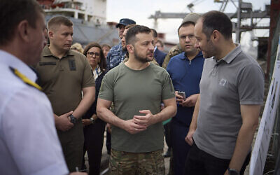 Ukrainian President Volodymyr Zelensky, center, surrounded by ambassadors of different countries and UN officials, visits a port in Chornomork during loading of grain on a Turkish ship, background, close to Odesa, Ukraine, July 29, 2022. (Ukrainian Presidential Press Office via AP)