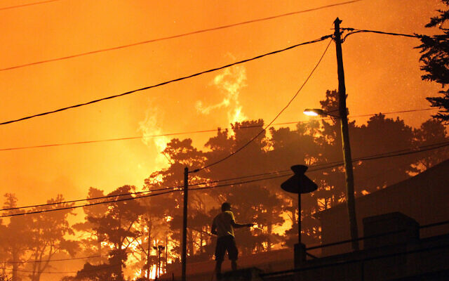 Illustrative: A man uses a garden hose to spray water on the roof of houses as forest fires rage nearby on the hills above the city of Funchal in the Portuguese Atlantic island of Madeira, July 18 2012. (AP/Joana Sousa) Illustrative: A man uses a garden hose to spray water on the roof of houses as forest fires rage nearby on the hills above the city of Funchal in the Portuguese Atlantic island of Madeira, July 18 2012. (AP/Joana Sousa)