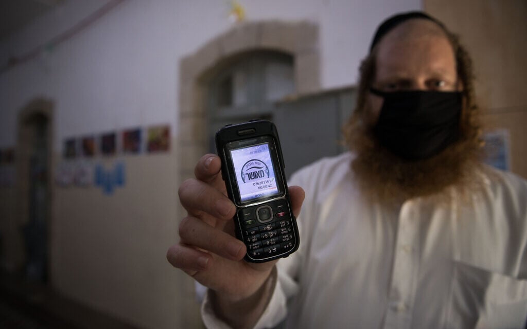 A man holds up his cellular phone certificating that it is 'kosher' at the entrance to an ultra-Orthodox school in Jerusalem on May 6, 2020. (Nati Shohat/ Flash90) A man holds up his cellular phone certificating that it is 'kosher' at the entrance to an ultra-Orthodox school in Jerusalem on May 6, 2020. (Nati Shohat/ Flash90)