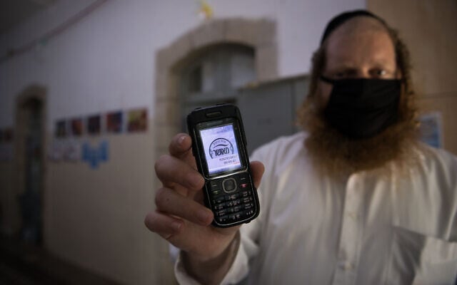 ILLUSTRATIVE: A man holds up his cellular phone certificating that it is 'kosher' at the entrance to an ultra-Orthodox school in Jerusalem on May 6, 2020. (Nati Shohat/ Flash90) ILLUSTRATIVE: A man holds up his cellular phone certificating that it is 'kosher' at the entrance to an ultra-Orthodox school in Jerusalem on May 6, 2020. (Nati Shohat/ Flash90)