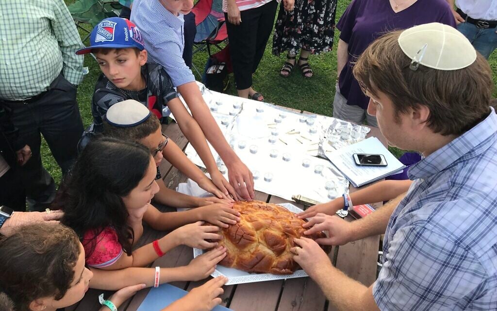 Rabbi Matt Abelson, right, makes the blessing over bread with children of the Jericho Jewish Center at Shabbat in the park, 2019. (Leslie Hartman) Rabbi Matt Abelson, right, makes the blessing over bread with children of the Jericho Jewish Center at Shabbat in the park, 2019. (Leslie Hartman)