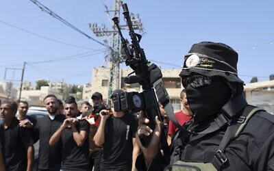 A gunman affiliated with the Palestinian Islamic Jihad terror group, marches as men carry the body of Dirar al-Kafrayni, killed during clashes with Israeli troops in the West Bank city of Jenin, during his funeral at the Jenin refugee camp, on August 2, 2022. (Jaafar Ashitiyeh/AFP)